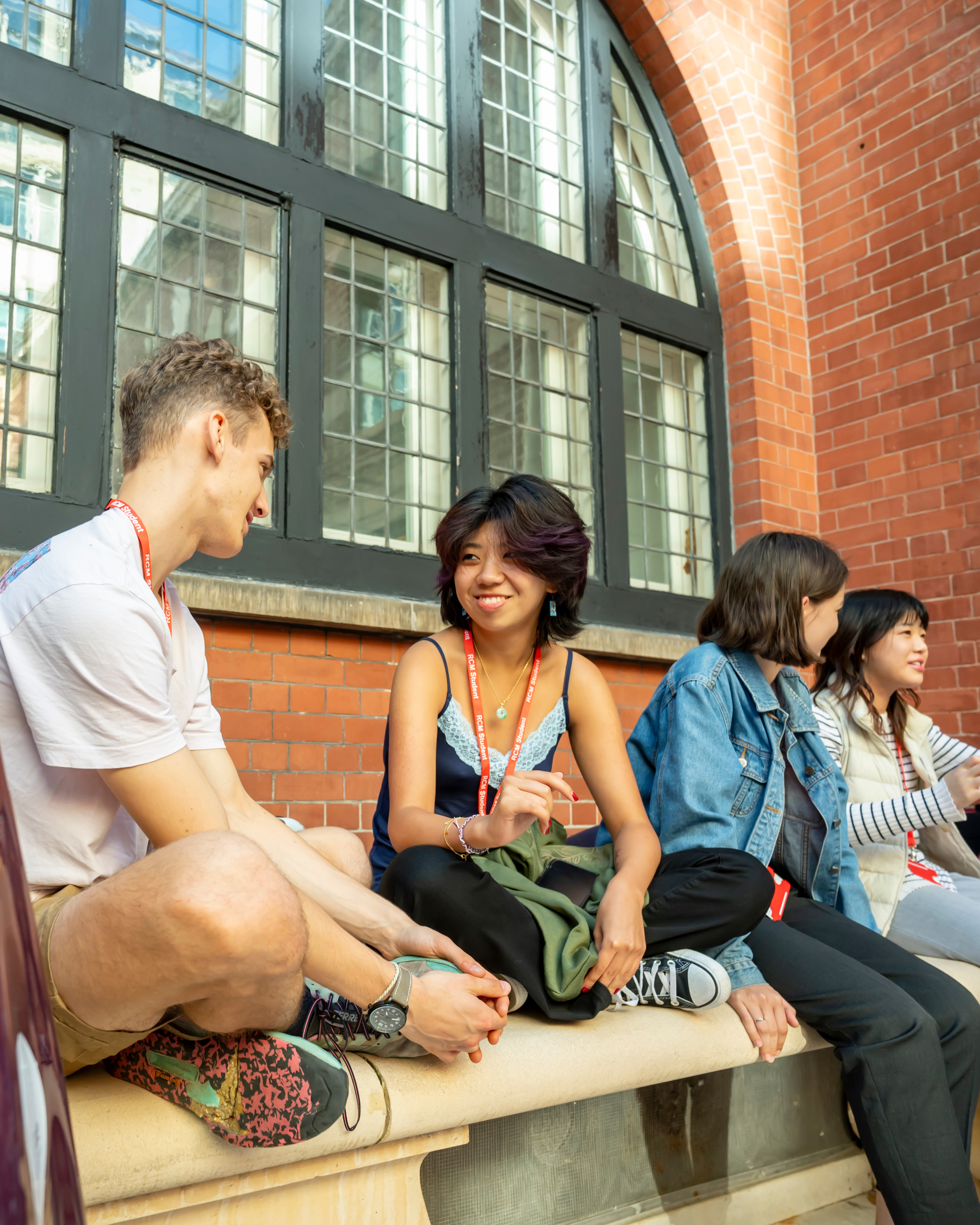 A group of students, chatting to each other, sitting on ledge in courtyard.